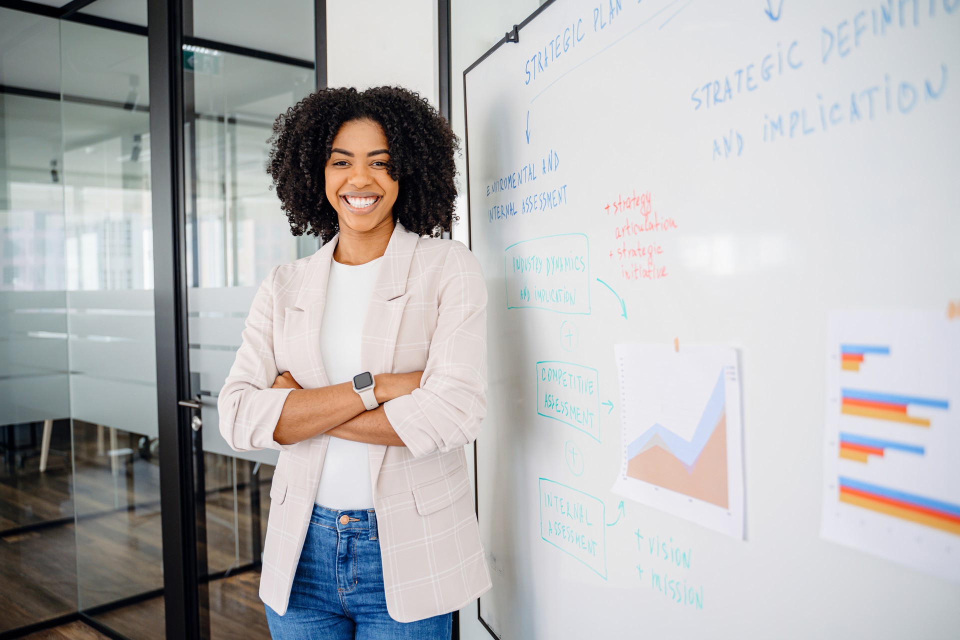 A confident female professional stands casually against a whiteboard